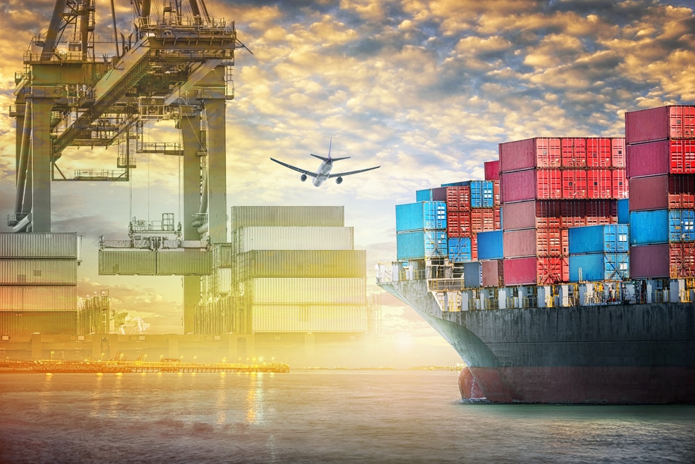 A cargo ship loaded with colorful shipping containers is docked at a port. Overhead cranes move containers, and an airplane flies above, illustrating global trade, logistics, and the efficiency of an agile supply chain.