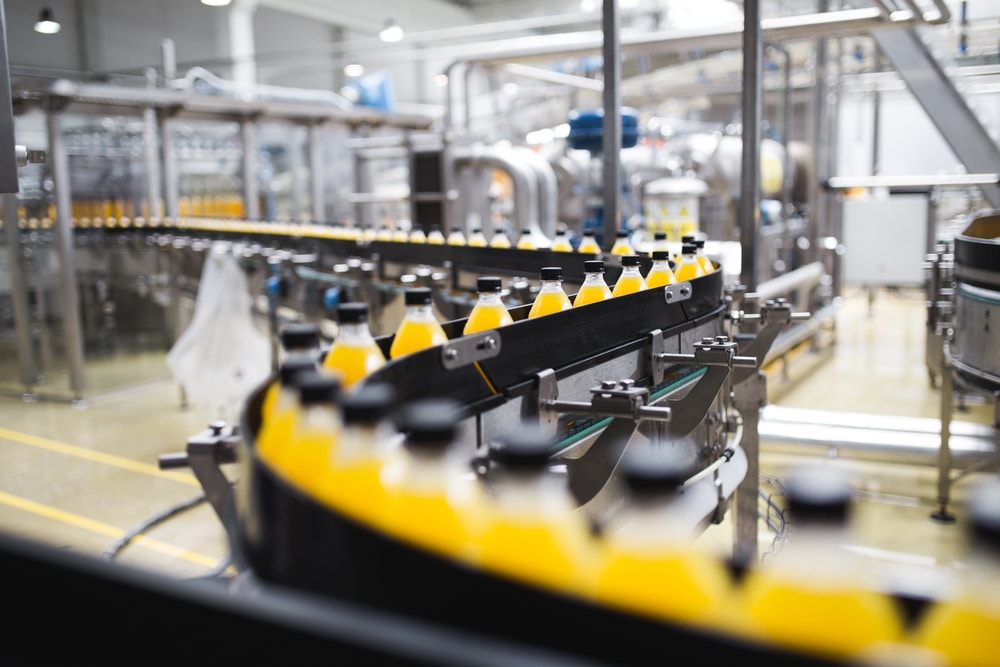 A bottling plant production line showcases automation strategies, with rows of yellow-capped bottles filled with orange liquid moving along conveyor belts in an industrial setting.