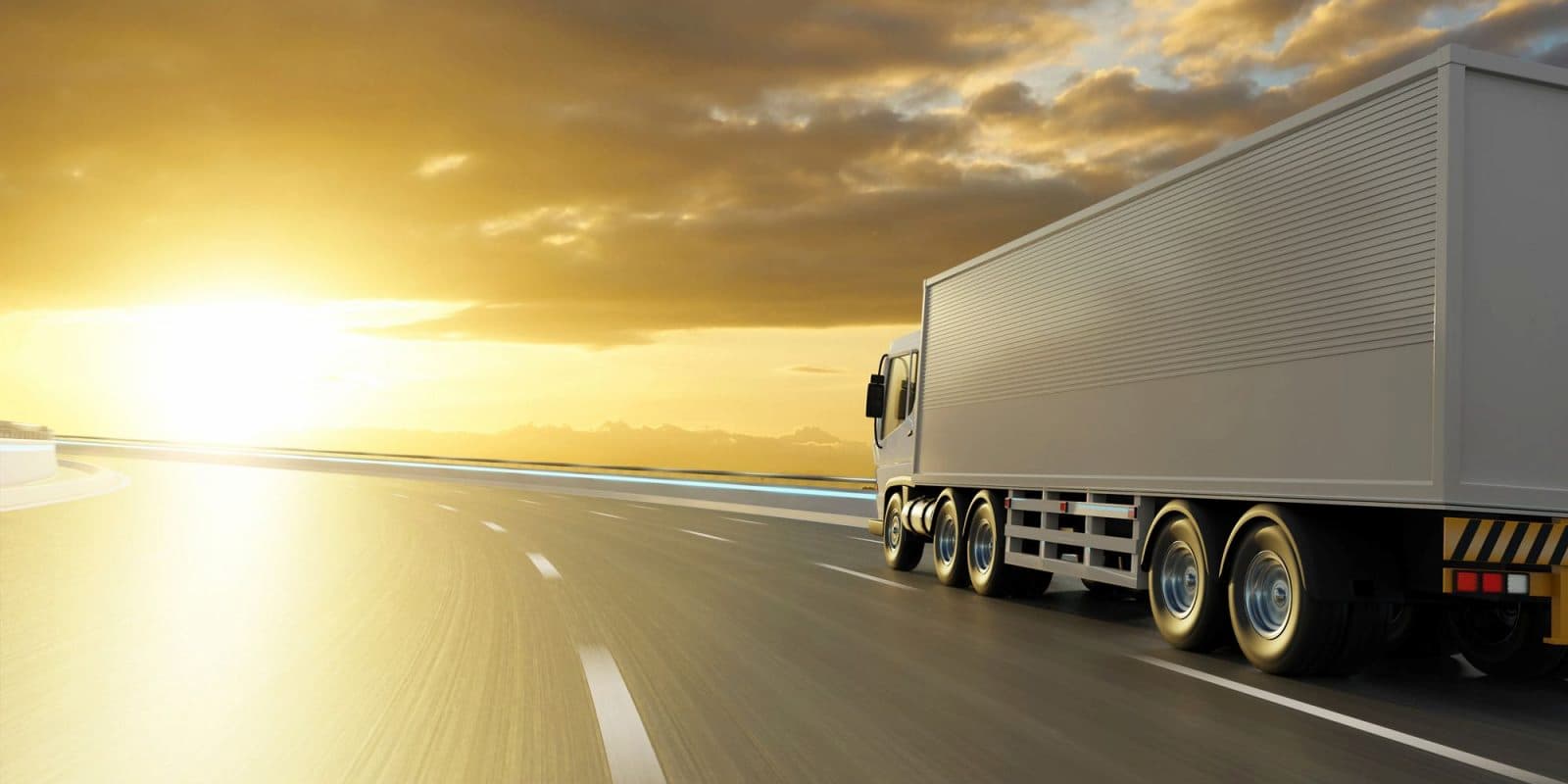 A large white truck drives on a highway toward the sunset under a cloudy sky, with sunlight reflecting off the road—undeterred by changing tariffs that shape its journey.