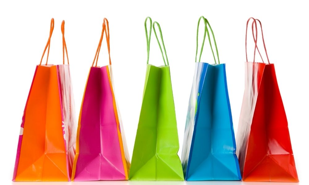 Five colorful shopping bags—orange, pink, green, blue, and red—stand upright in a row against a white background, their handles visible at the top. A vibrant display ideal for showcasing modern retail solutions.