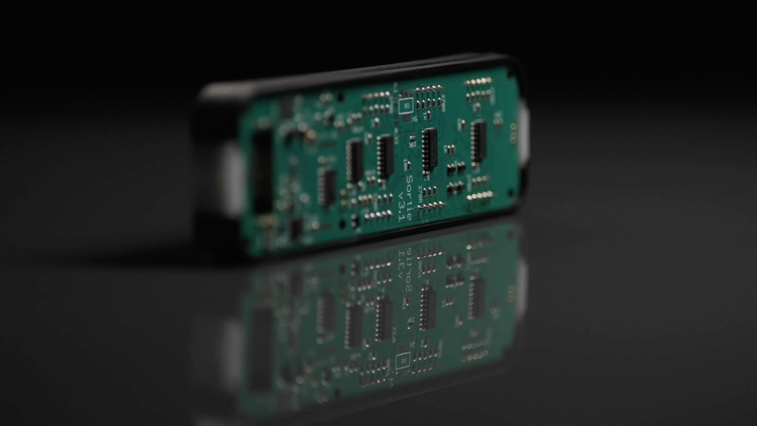 A close-up of a green electronic circuit board with various small components, standing on its edge and reflected on a glossy black surface.