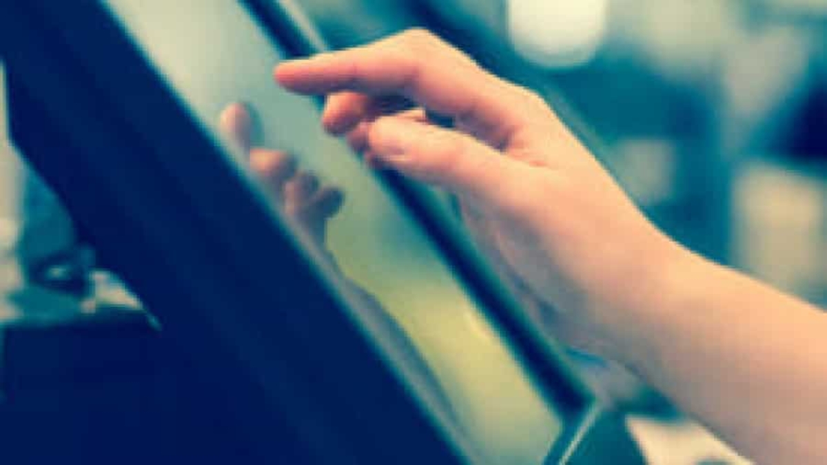 A close-up of a hand touching the screen of a touchscreen device, likely a kiosk or tablet, with a blurred background.