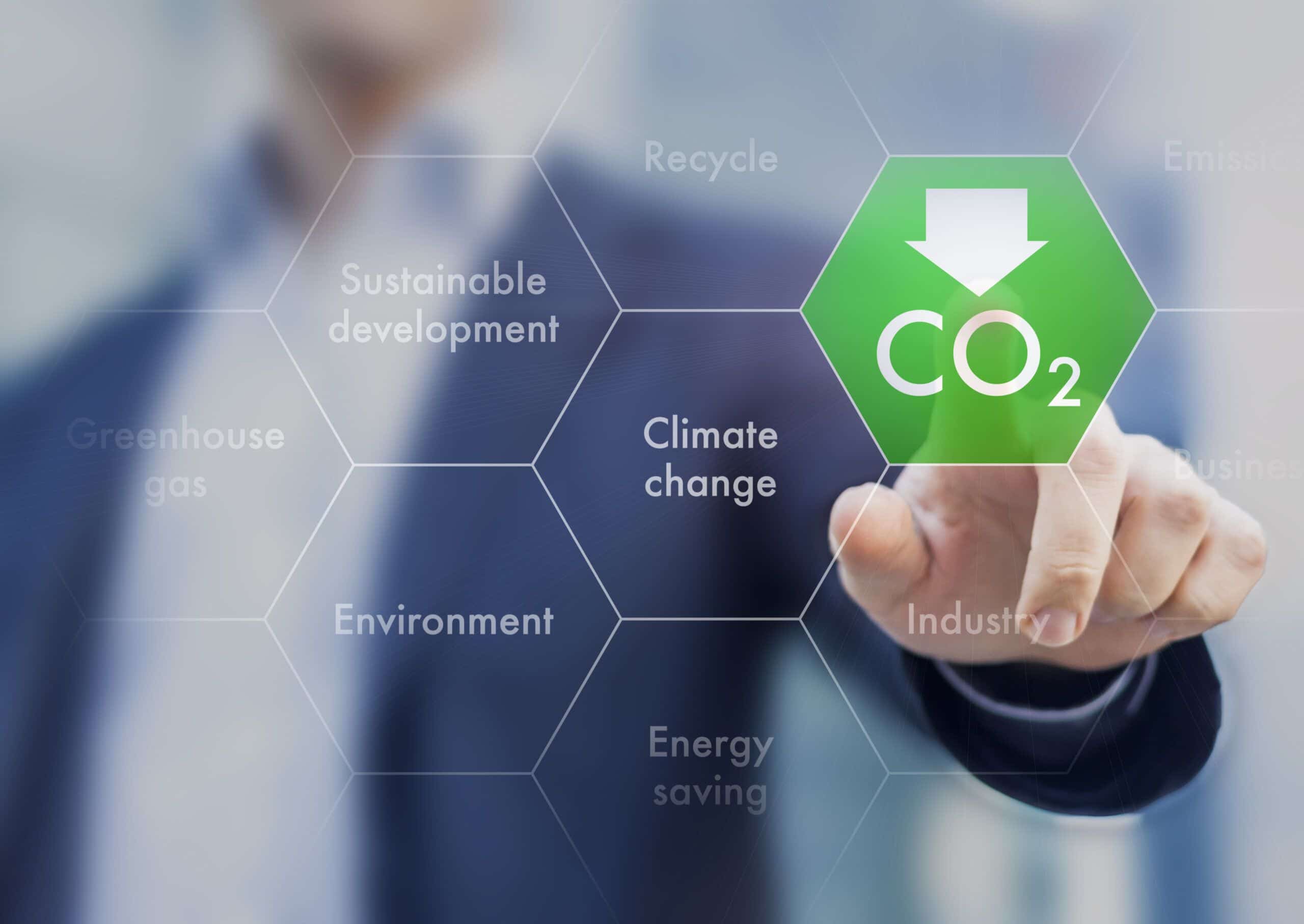 A person presses a digital hexagon labeled CO₂ with a downward arrow on a transparent screen. Surrounding hexagons display words like Climate change, Sustainable development, and Environment.