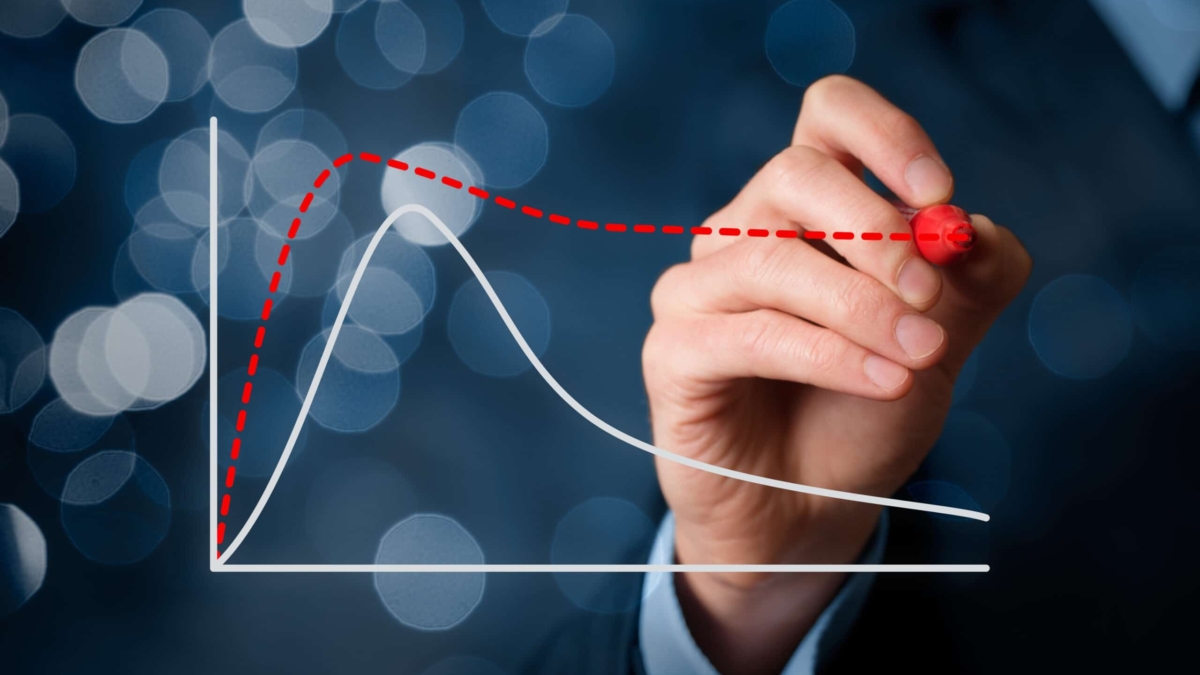 A hand in a suit draws a red dashed trend line above a white line graph on a transparent screen, with blurred blue lights in the background.