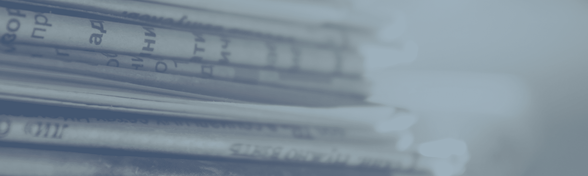 A close-up view of a stack of newspapers, with printed text visible on the pages. The image has a blue tint and a blurred background.