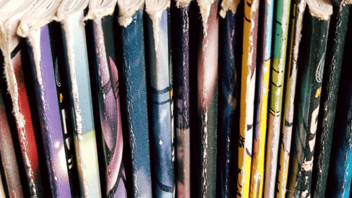Close-up view of the top edges and spines of several colorful comic books or graphic novels lined up vertically on a shelf.