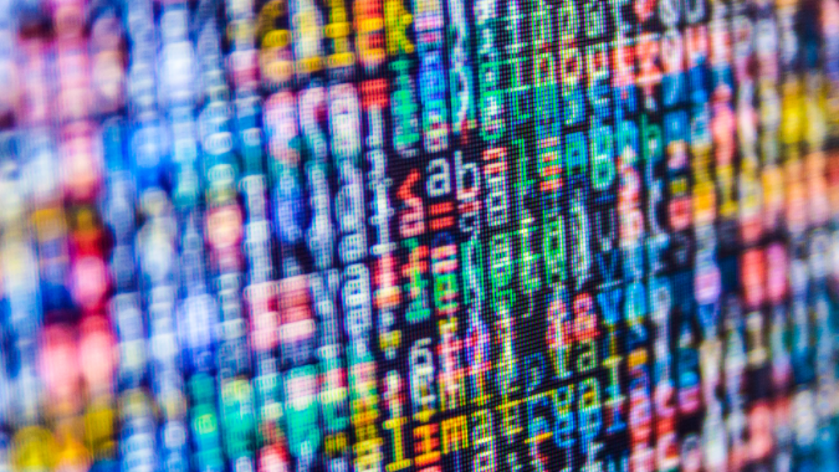 A close-up of a computer screen displaying colorful, blurred lines of programming code in various colors, including blue, green, red, and yellow, creating an abstract, pixelated effect.