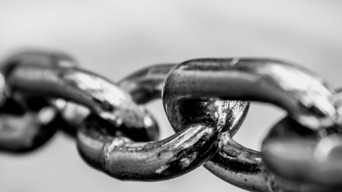 Close-up black and white photo of a metal chain, focusing on several interlinked, shiny chain links with a blurred background.