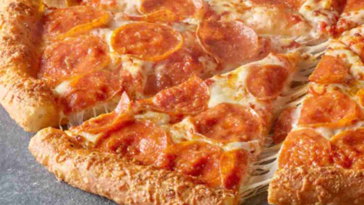 A close-up of a pepperoni pizza with melted cheese and a golden, thick crust. One slice is being pulled away, showing stretchy cheese between the slice and the rest of the pizza.