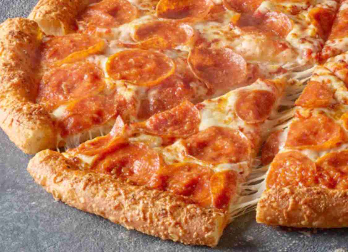 A close-up of a pepperoni pizza with melted cheese and a golden, thick crust. One slice is being pulled away, showing stretchy cheese between the slice and the rest of the pizza.