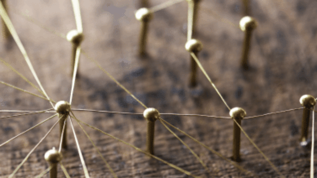 Close-up of golden pins connected by thin threads, arranged on a wooden surface to form a network or web-like pattern representing interconnectedness.