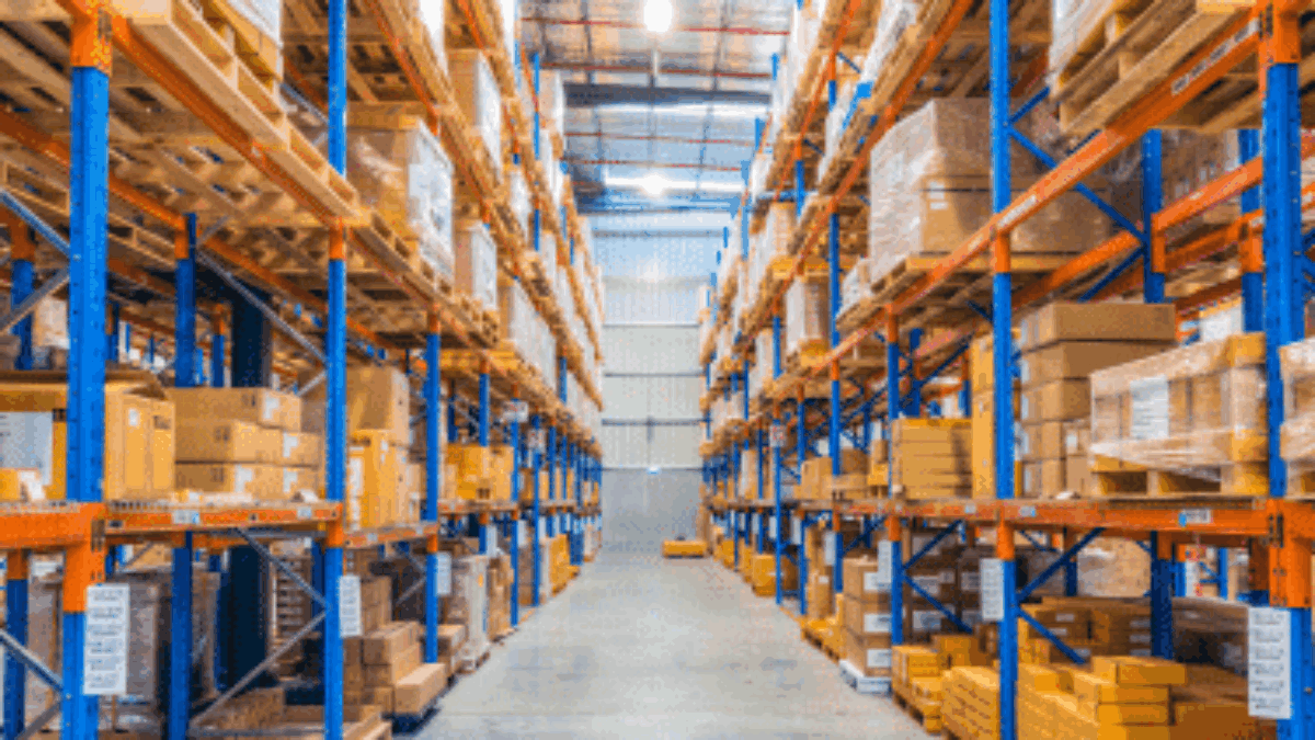 A brightly lit warehouse with tall shelves stacked with neatly organized boxes and packages, creating clear aisles for easy access—showcasing what slotting can achieve in maximizing storage efficiency and workflow.