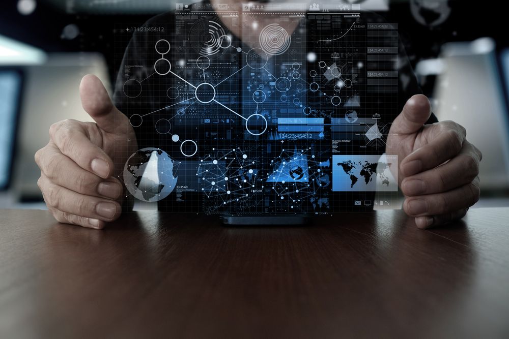 Person holding hands around a table with a digital interface of futuristic graphs, data charts, and network connections projected in the air above a mobile device.