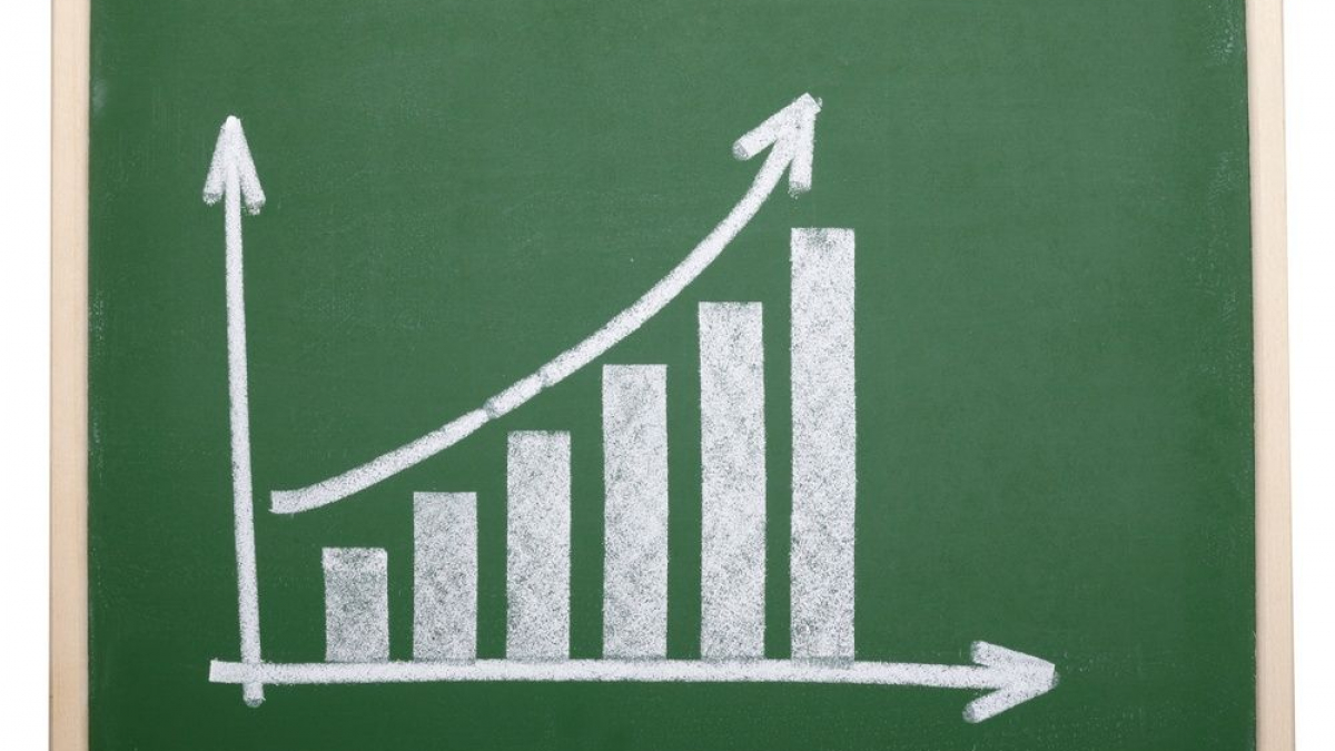 A chalk drawing on a green chalkboard shows an upward trending bar graph with an arrow, indicating growth or progress. The board is framed with light-colored wood.