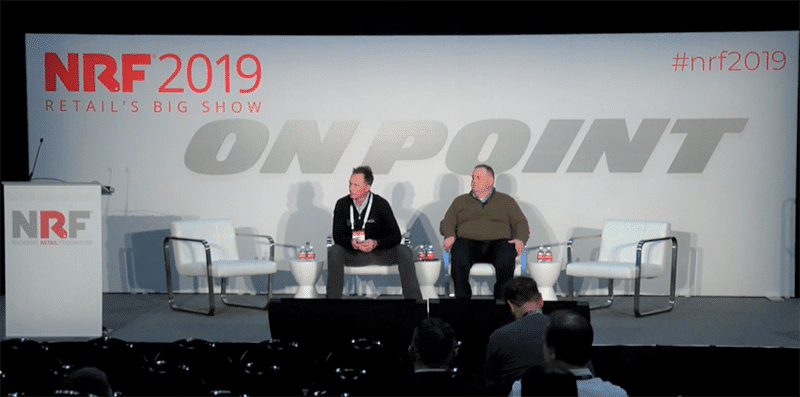 nrf presentation cover_vendor drop ship 800w Two men sit on a stage with three empty chairs at NRF 2019 Retail’s Big Show. The backdrop has “ON POINT” and event branding. A podium is on the left, and a few people are seated in the audience.