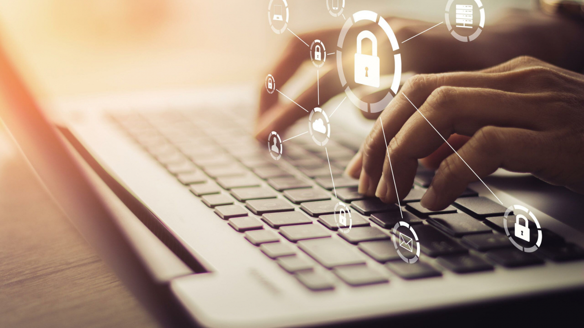 Hands typing on a laptop keyboard with security and technology icons, including a padlock and network symbols, digitally overlaid to represent cybersecurity and data protection.