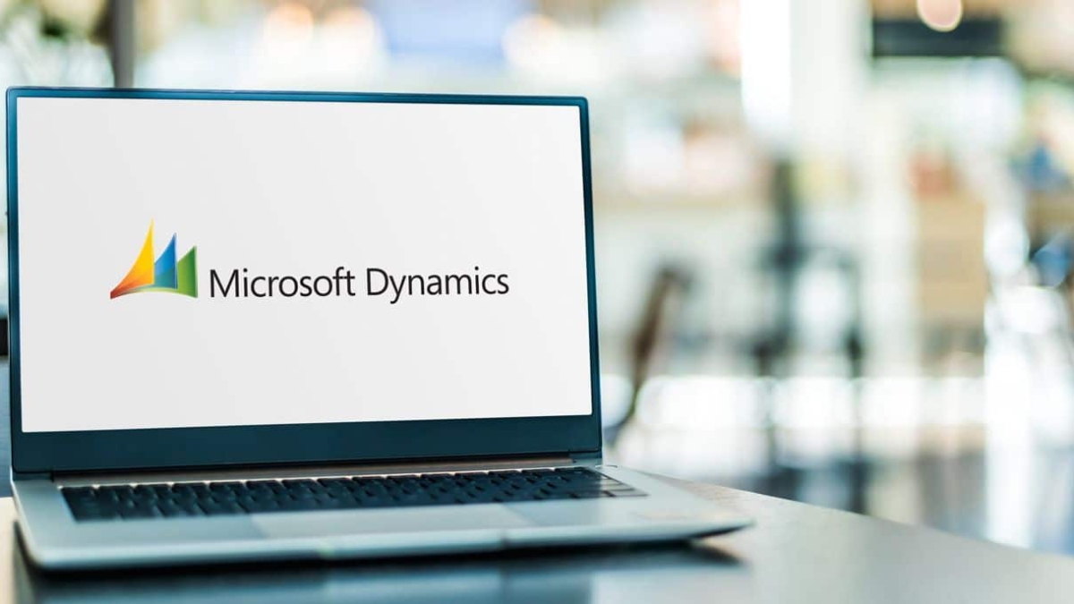 A laptop on a table displays the Microsoft Dynamics logo on its screen, with a blurred indoor background.