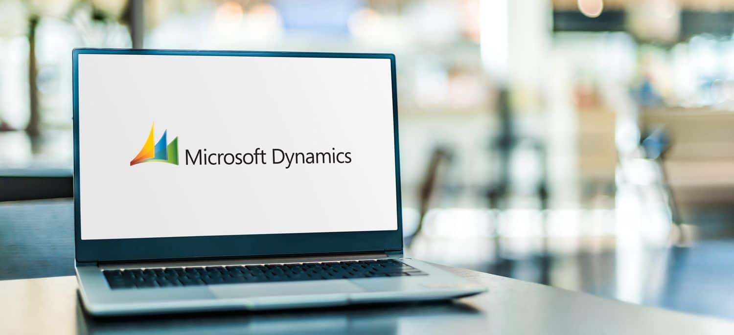 A laptop on a table displays the Microsoft Dynamics logo on its screen, with a blurred indoor background.