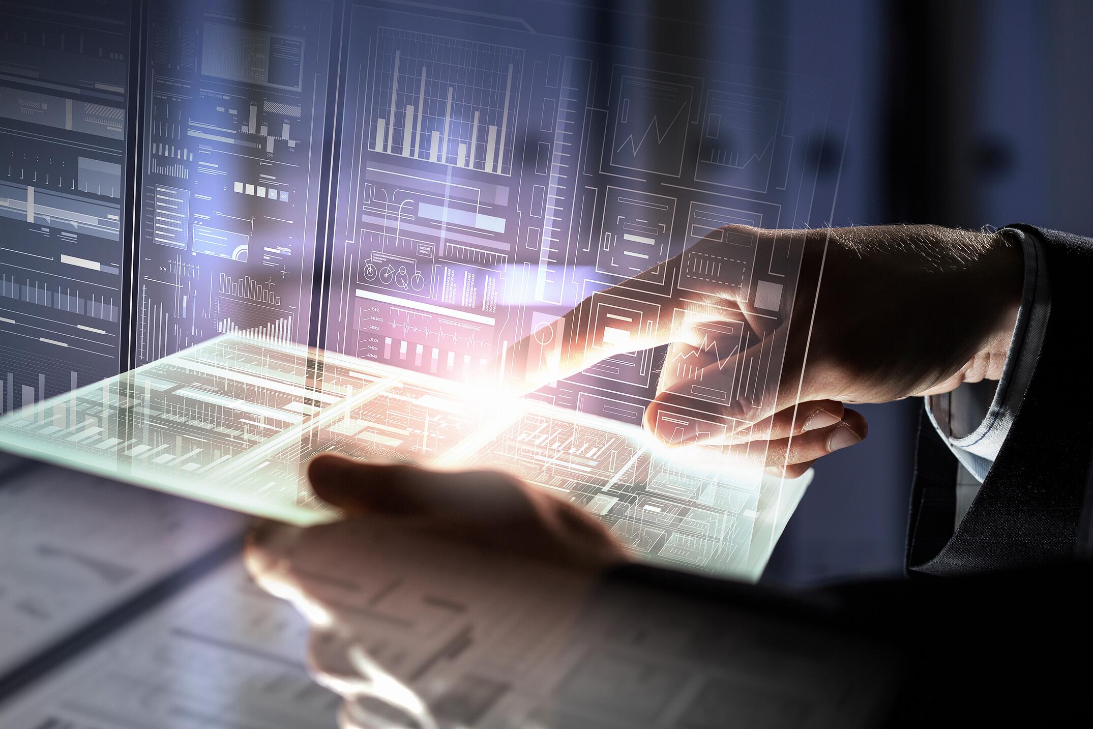 A person’s hand interacts with a glowing transparent tablet, surrounded by futuristic digital data displays and graphs, symbolizing advanced technology and data analysis.
