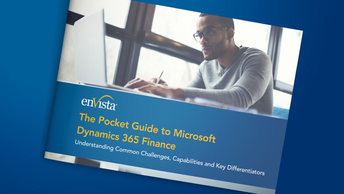 A man wearing glasses works on a laptop near large windows. The image shows a booklet titled The Pocket Guide to Microsoft Dynamics 365 Finance by enVista, with a subtitle about challenges, capabilities, and differentiators.