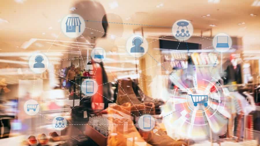 image – 2025-04-09T182506.382 A blurred retail store with shoes and clothes displays, overlaid with digital shopping icons like a shopping cart, store, and user profiles, representing online and in-store shopping integration.