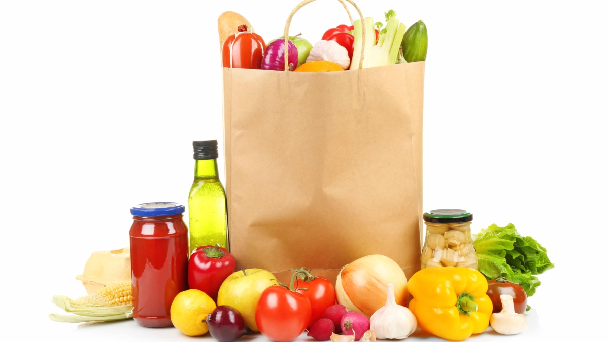 A paper grocery bag filled with fresh vegetables and bread sits on a white background, surrounded by produce like tomatoes and onions—ideal for showcasing effective distribution consulting in food retail.