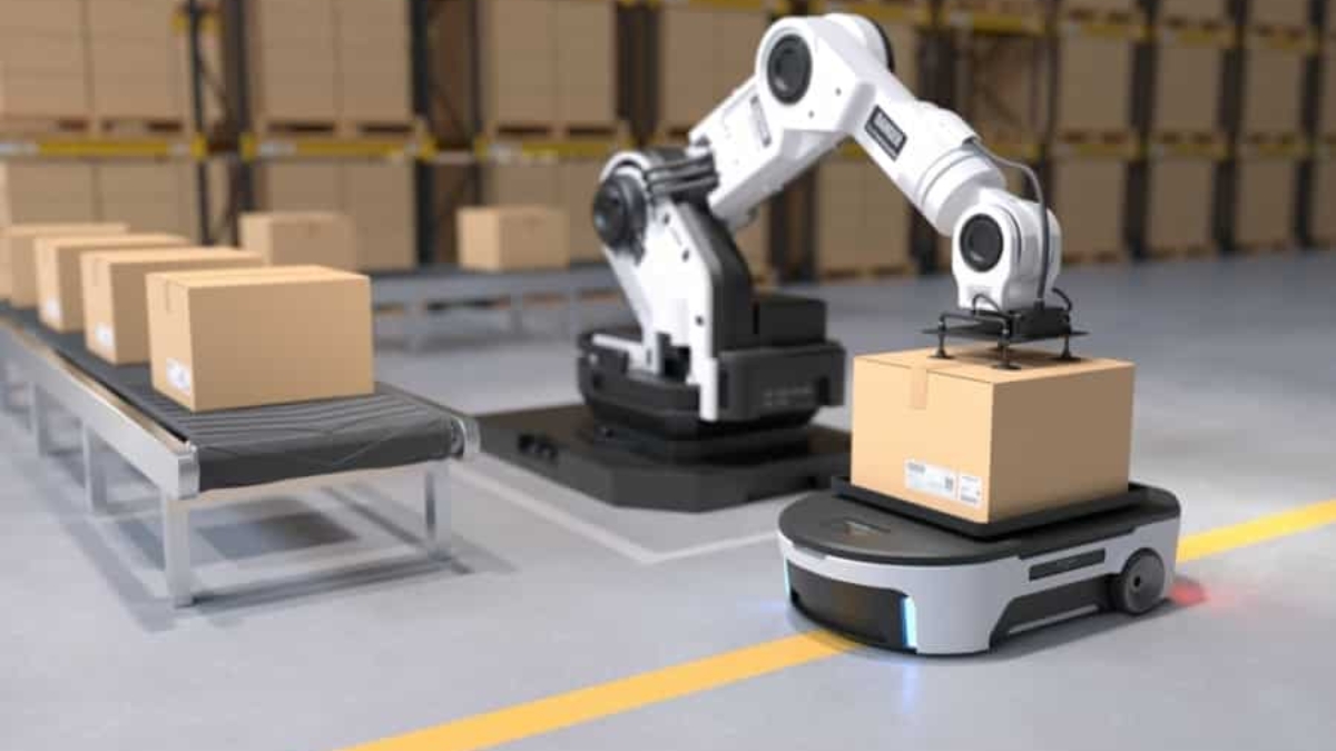 A robotic arm places a cardboard box onto a mobile robot in a warehouse, offering a glimpse into the future of supply chain, with shelves of boxes in the background and a conveyor belt carrying more boxes on the left side.