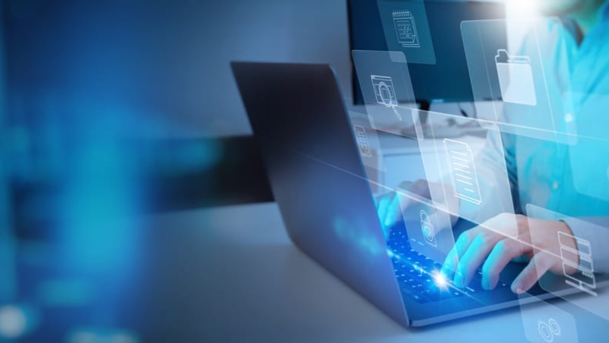 Person typing on a laptop with holographic icons for files, folders, and data storage, symbolizing digital data management and the comparison of business central vs finance and supply chain management in information technology.