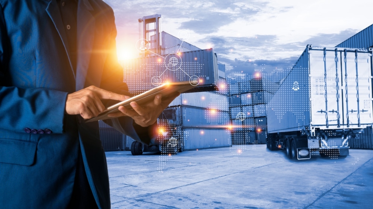 A person in a suit uses a tablet at a shipping yard with stacked cargo containers and a truck. Digital network graphics overlay the scene, highlighting advanced supply chain planning and logistics technology.