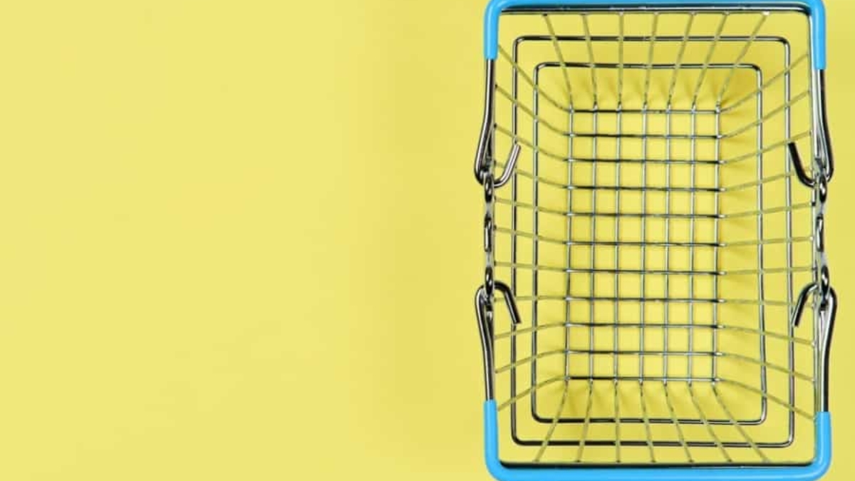 A small, empty metal shopping basket with blue handles sits on a yellow background, viewed from above.