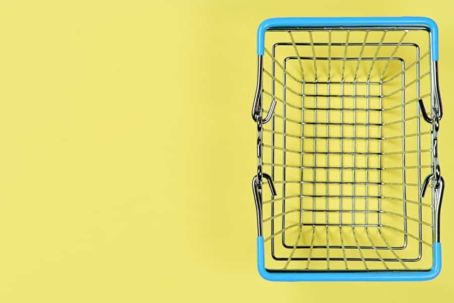 A small, empty metal shopping basket with blue handles sits on a yellow background, viewed from above.