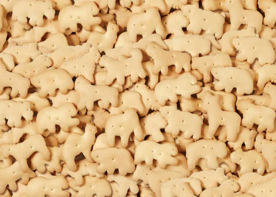 A pile of assorted animal-shaped cookies, known as animal crackers, featuring various animal designs in light golden brown color.