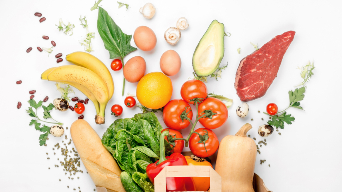 A paper bag filled with fresh vegetables, fruits, bread, and eggs is surrounded by assorted foods—each showcasing supply chain traceability—including bananas, tomatoes, spinach, steak, avocado, oranges, mushrooms, and quail eggs on a white background.