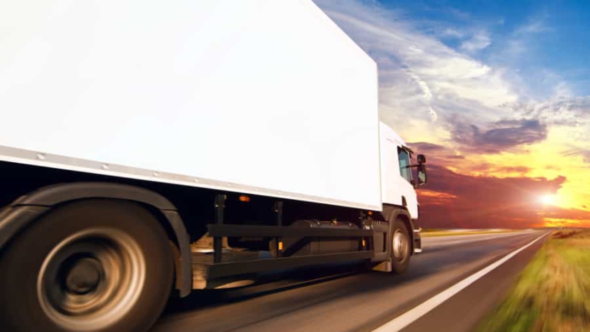 A white delivery truck speeds down a highway at sunset, framed by dramatic blue, orange, and yellow skies—a striking scene that captures the efficiency powered by modern transportation software.