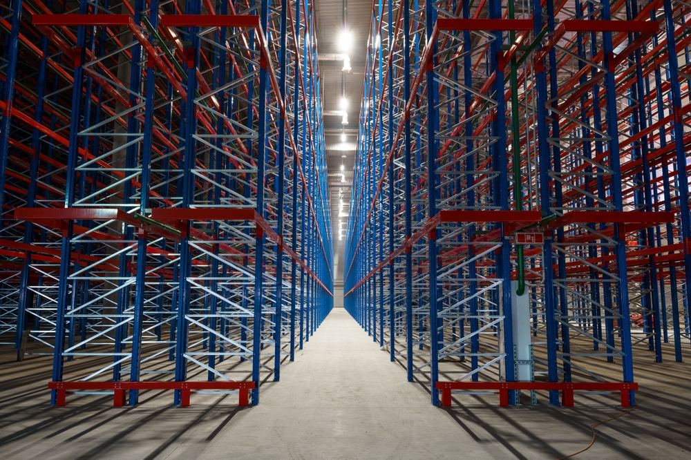 Symmetrical,Warehouse,Racking,System,With,Metal,Frames Empty metal storage racks extend in symmetrical rows inside a large warehouse, creating a sense of depth and perspective—an ideal setting for ai-powered inventory systems. Bright lights illuminate the clean concrete floor and steel framework.