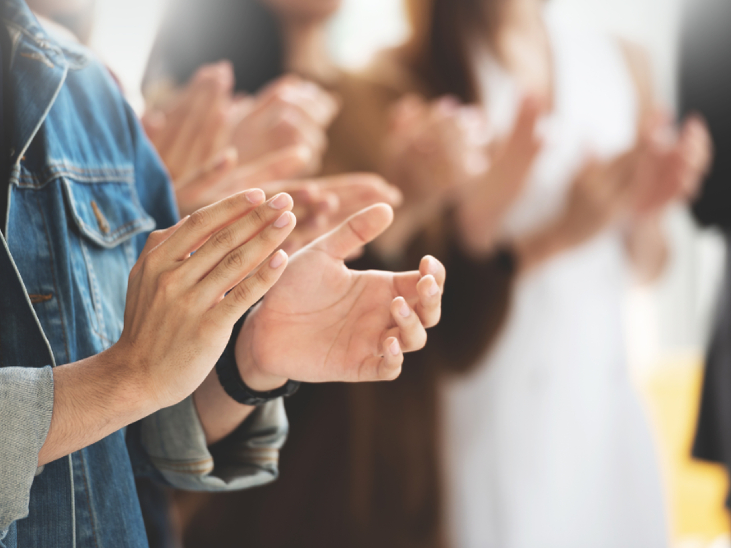 A close-up of several people clapping, with hands in focus and blurred figures in the background. The group appears to be applauding during an enVista Careers event or indoor gathering.